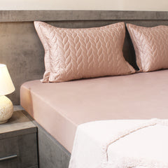 Bed with pink quilted pillows and matching bedding in a bedroom setting.