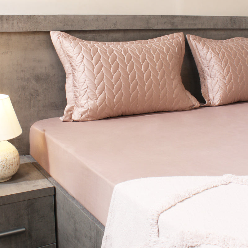 Bed with pink quilted pillows and matching bedding in a bedroom setting.