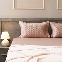 Neatly made bed with pink textured pillows and a matching blanket, nightstand with lamp on the side.