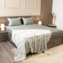 Bedroom with a neatly made bed featuring a green comforter and pillows, with nightstands and lamps.