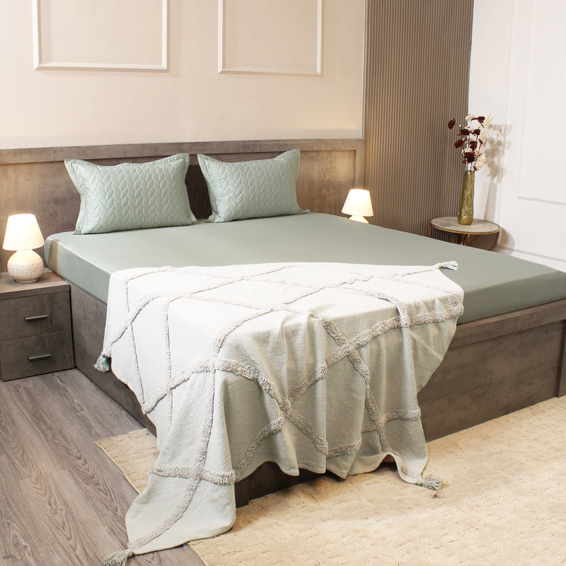 Bedroom with a neatly made bed featuring a green comforter and pillows, with nightstands and lamps.