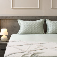 Neatly made bed with light green bedding and pillows in a bedroom setting.