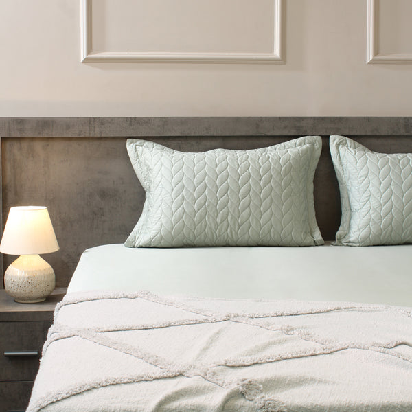 Neatly made bed with light green bedding and pillows in a bedroom setting.