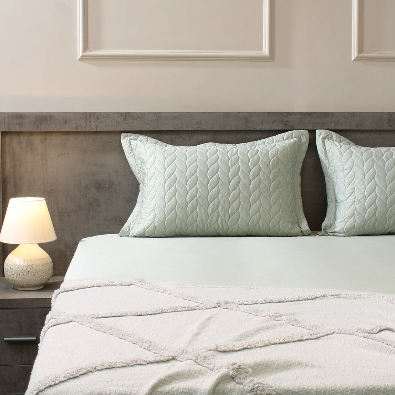 Neatly made bed with light green bedding and pillows in a bedroom setting.