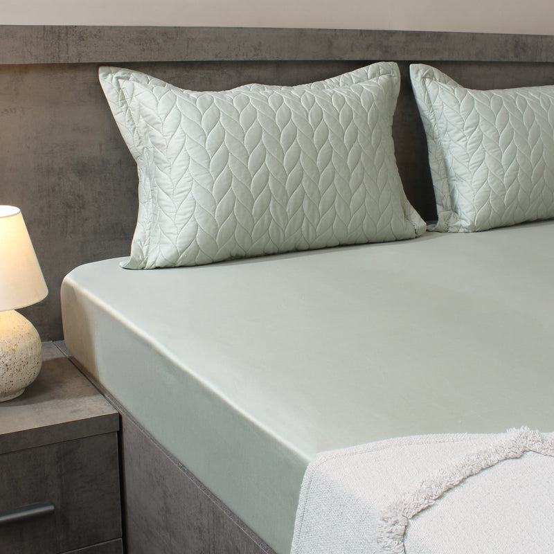 Bed with light green bedding and textured pillows in a bedroom setting.