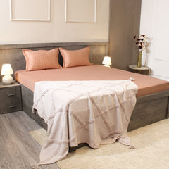 Bedroom with a bed featuring pink bedding and a beige blanket, nightstands with lamps, and a vase on a shelf.