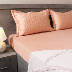 Bed with pink bedding and pillows in a bedroom setting.