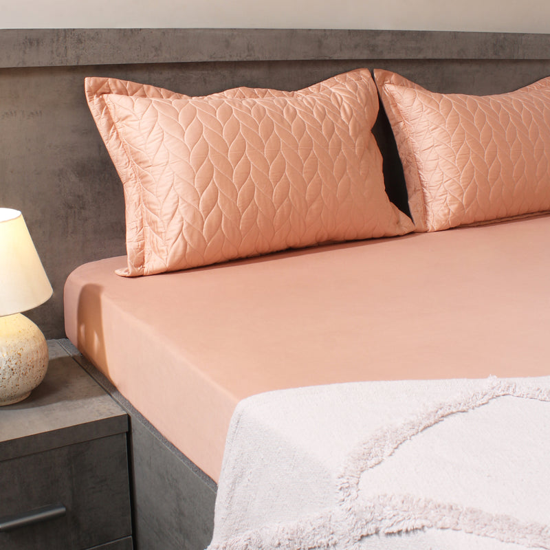 Bed with pink bedding and pillows in a bedroom setting.