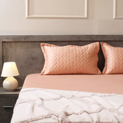 Bed with pink bedding and pillows, nightstand with lamp, neutral wall