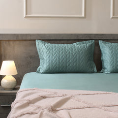 Teal bedding set with matching pillows on a bed in a bedroom setting.