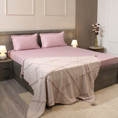 Bedroom with a bed featuring pink bedding and a beige blanket, nightstands with lamps, and decorative elements.