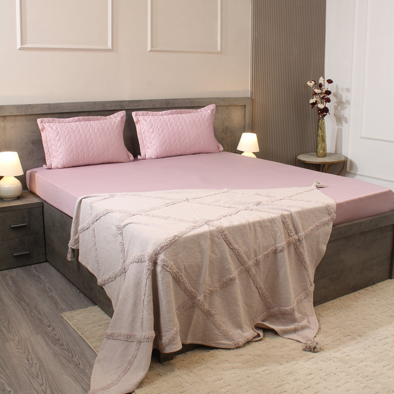 Bedroom with a bed featuring pink bedding and a beige blanket, nightstands with lamps, and decorative elements.