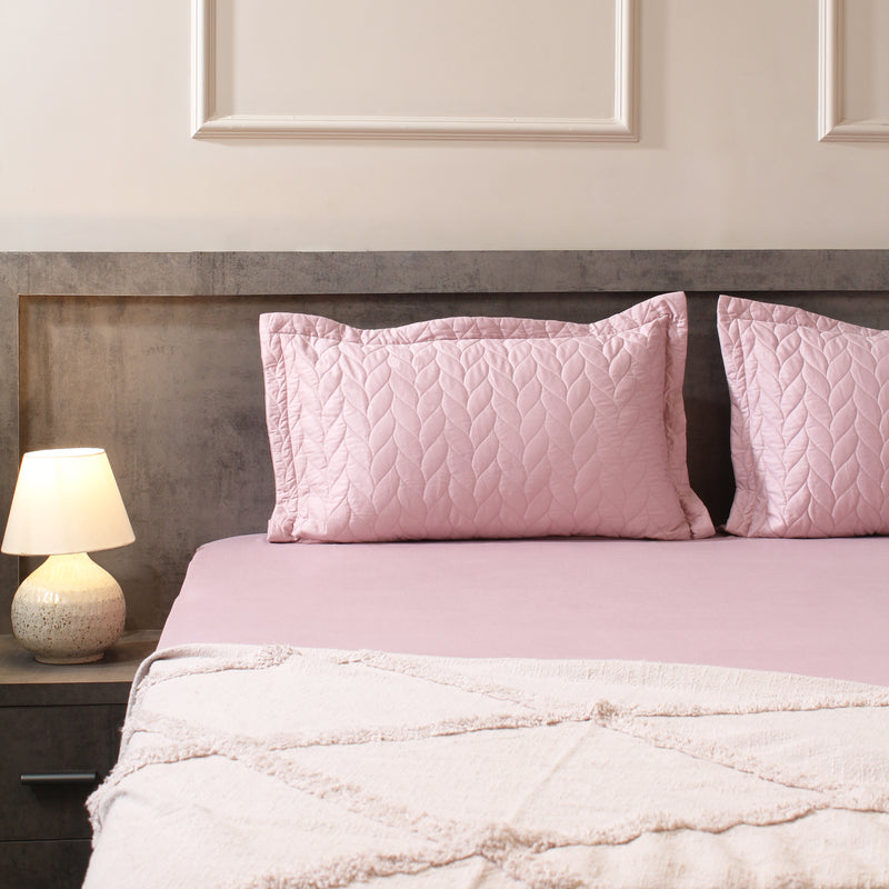 Pink quilted pillows on a bed with a matching pink comforter, against a neutral wall.