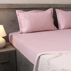 Pink quilted pillows on a bed with a matching pink fitted sheet in a bedroom setting.