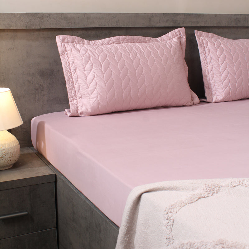 Pink quilted pillows on a bed with a matching pink fitted sheet in a bedroom setting.