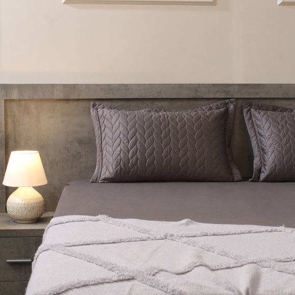 Gray bedding set with textured pillows on a bed in a bedroom setting.