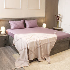 Bedroom with a bed featuring pink bedding and a beige blanket, two nightstands with lamps, and a vase on a shelf.