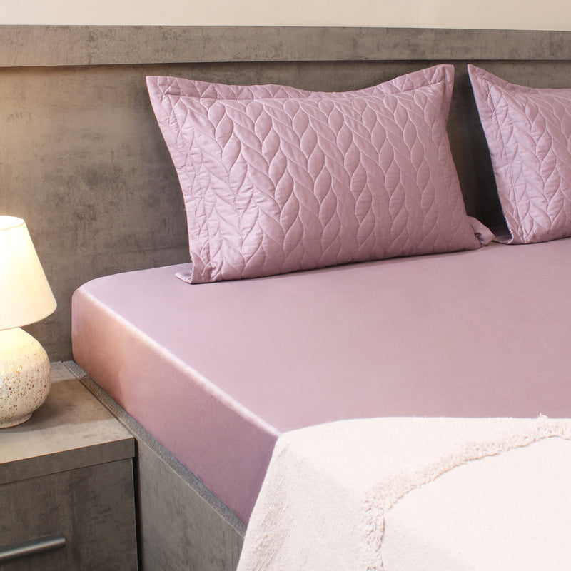 Pink quilted pillows on a bed with a neutral headboard and nightstand.