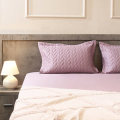 Bed with pink pillows and a nightstand with a lamp in a bedroom setting