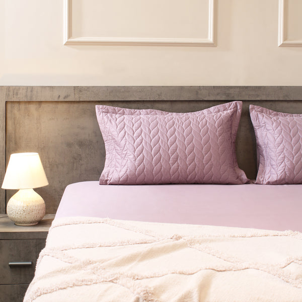 Bed with pink pillows and a nightstand with a lamp in a bedroom setting