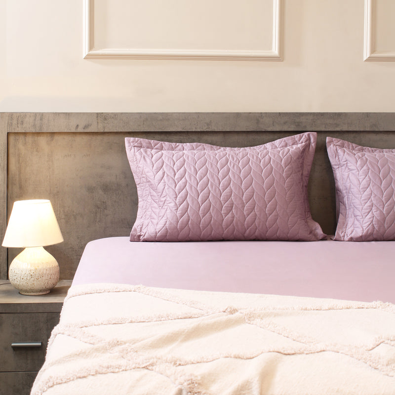 Bed with pink pillows and a nightstand with a lamp in a bedroom setting