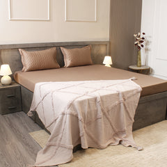 Neatly made bed with beige bedding and a decorative throw blanket in a bedroom setting.