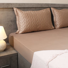 Beige bed sheets and pillows on a bed with a lamp on a nightstand.
