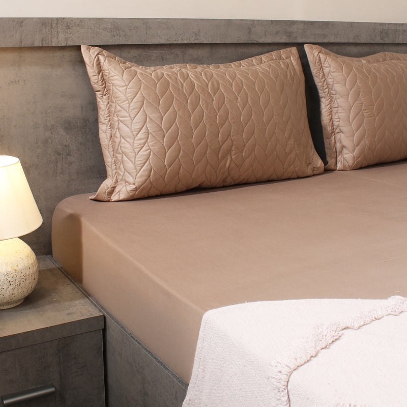 Beige bed sheets and pillows on a bed with a lamp on a nightstand.