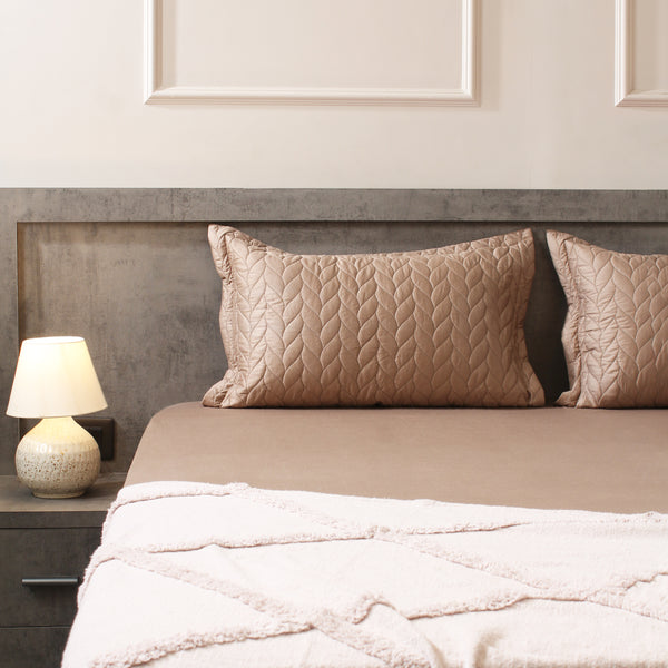 Neatly made bed with beige pillows and a lamp on a nightstand in a bedroom.