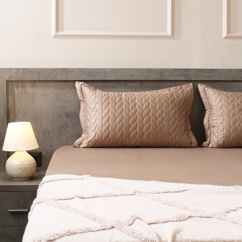Neatly made bed with beige pillows and a lamp on a nightstand in a bedroom.