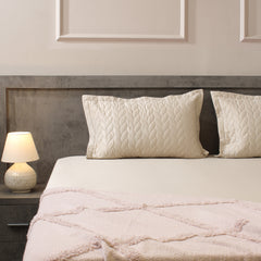 Neatly made bed with textured bedding and pillows in a bedroom setting.