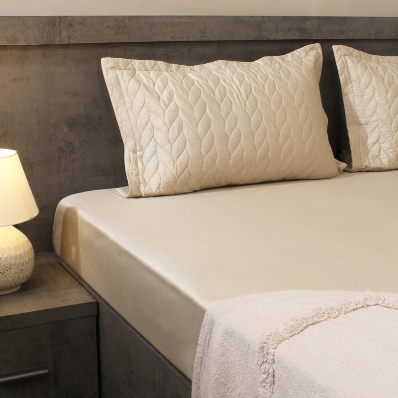 Neatly made bed with textured pillows and a lamp on a nightstand in a bedroom setting.