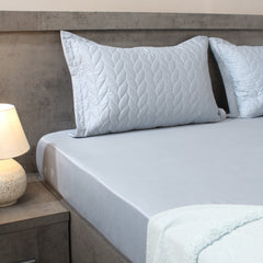 Bed with light blue bedding and pillows in a bedroom setting.