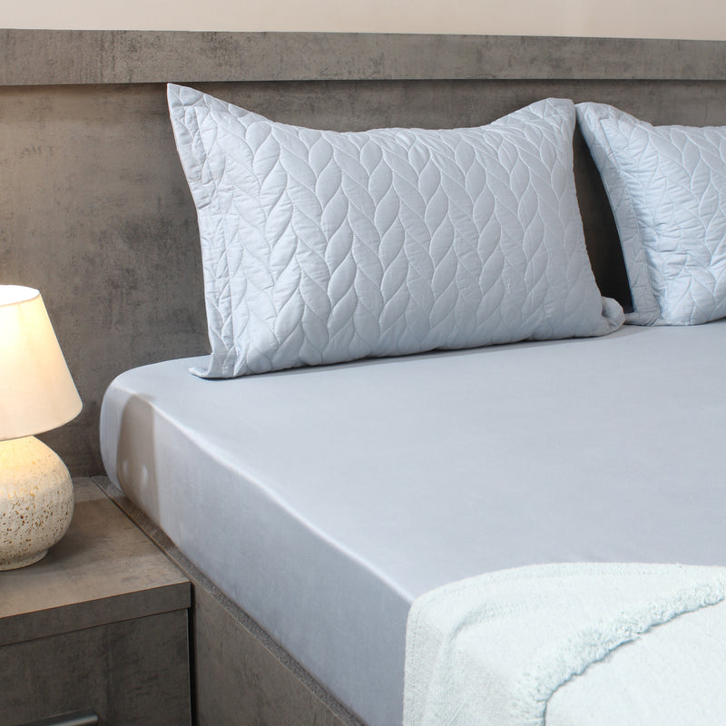 Bed with light blue bedding and pillows in a bedroom setting.