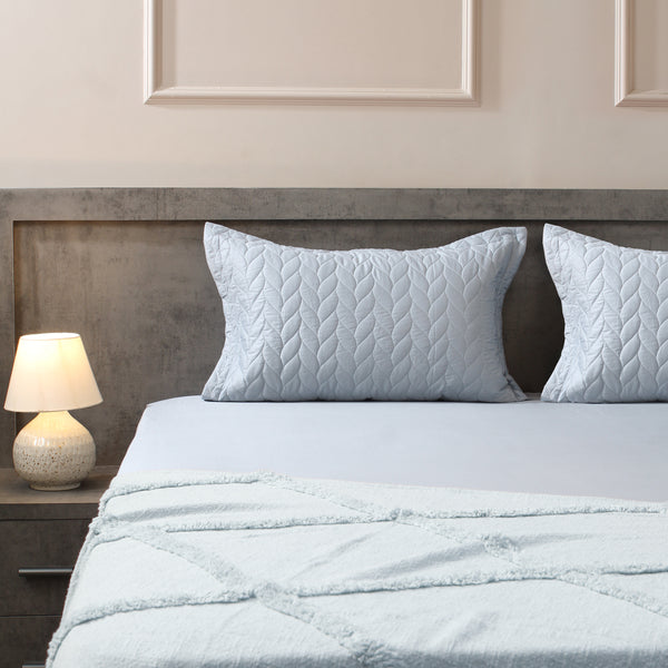 Light blue quilted bedding set on a bed with a lamp on a nightstand.