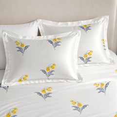 Floral embroidered pillows on a bed with a neutral headboard.