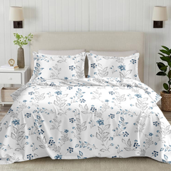 Floral-patterned bedding set on a bed in a bedroom setting with plants and lamps.