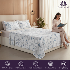 Woman reading a book by a bed with floral bedding, Casa Vaas brand visible