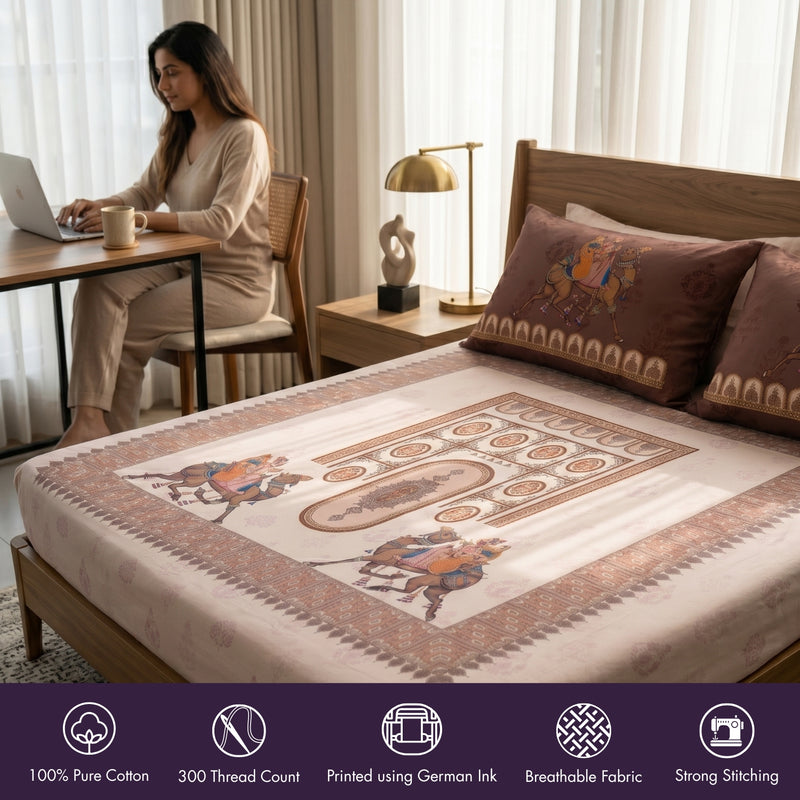 Woman working on a laptop at a desk with a bed featuring embroidered bedding in the foreground.