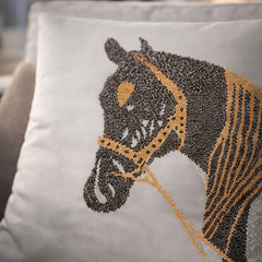 Gray pillow with a horse head design made of beads on a couch.